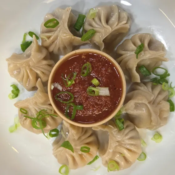 Paneer momo arranged around a bowl of house chutney, scattered with scallion