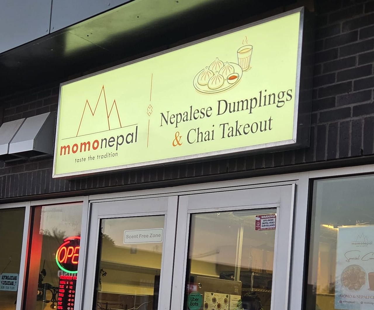 The MomoNepal storefront sign, reading Nepalese Dumplings and Chai Takeout, above the shop's glass doors