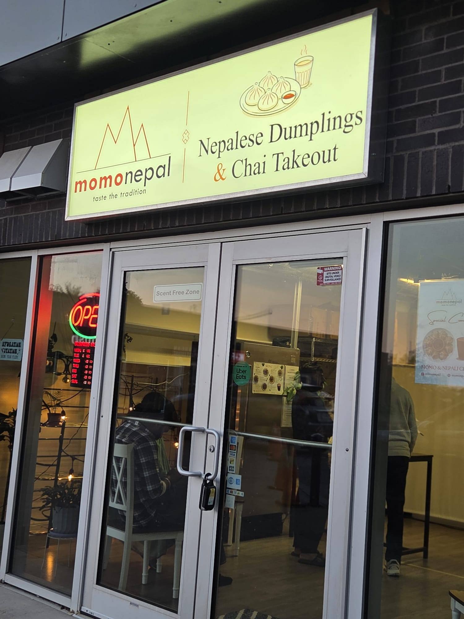 The MomoNepal storefront sign, reading Nepalese Dumplings and Chai Takeout, above the shop's glass doors